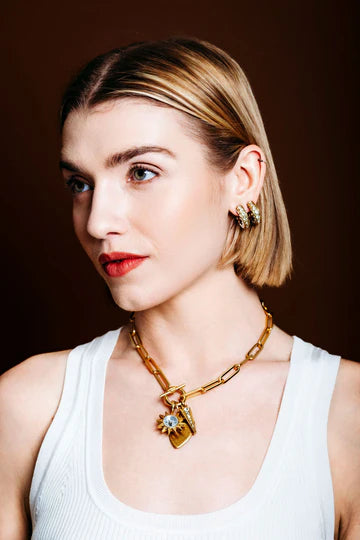 Woman wearing a gold elizabeth cole necklace with charms against a dark background