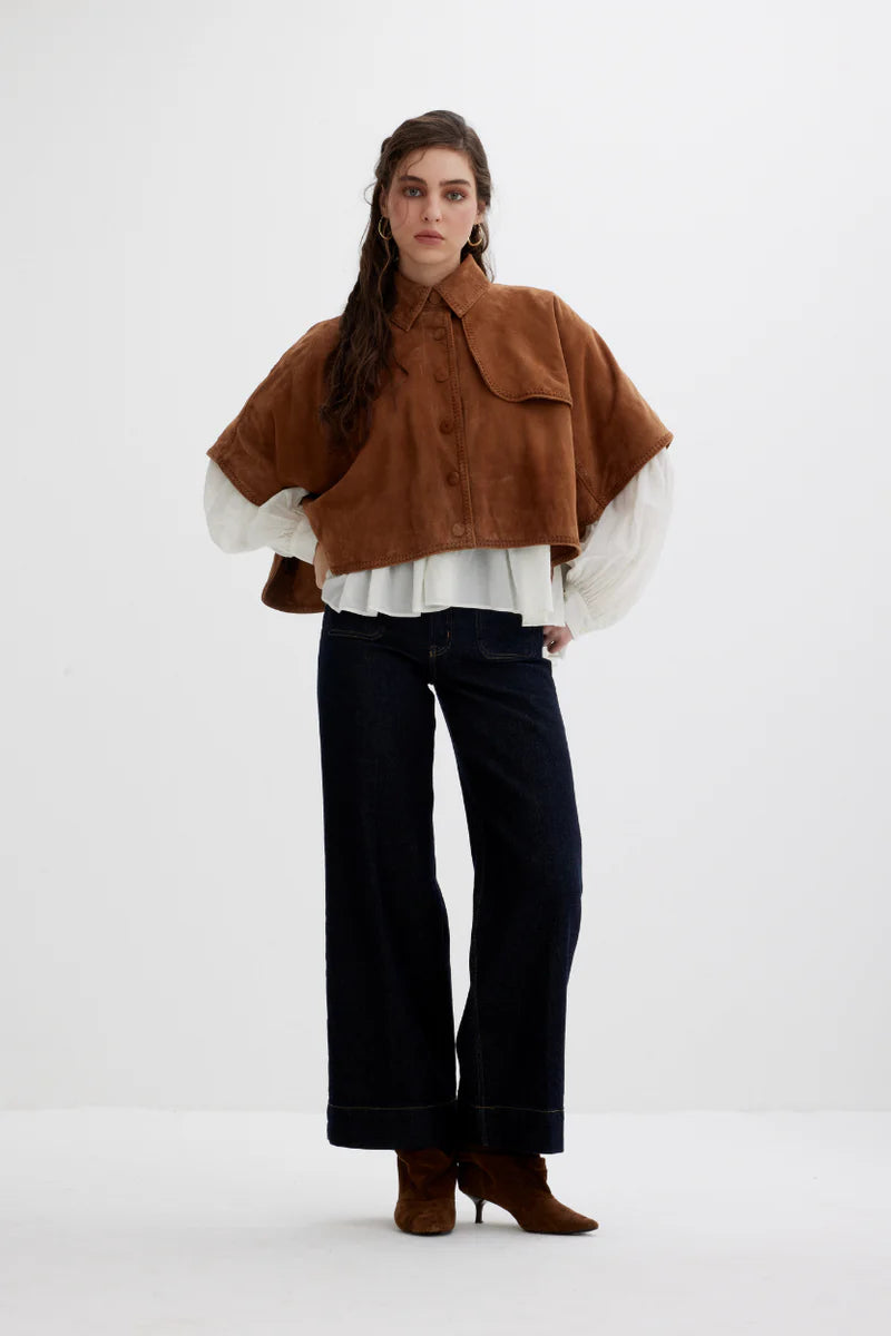 Woman wearing a brown poncho over a white shirt with black pants on a white background