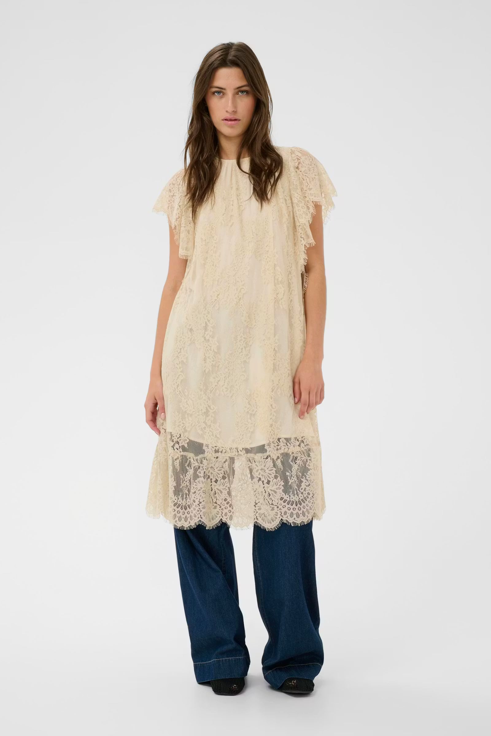 Woman wearing a beige lace dress with blue pants on a white background