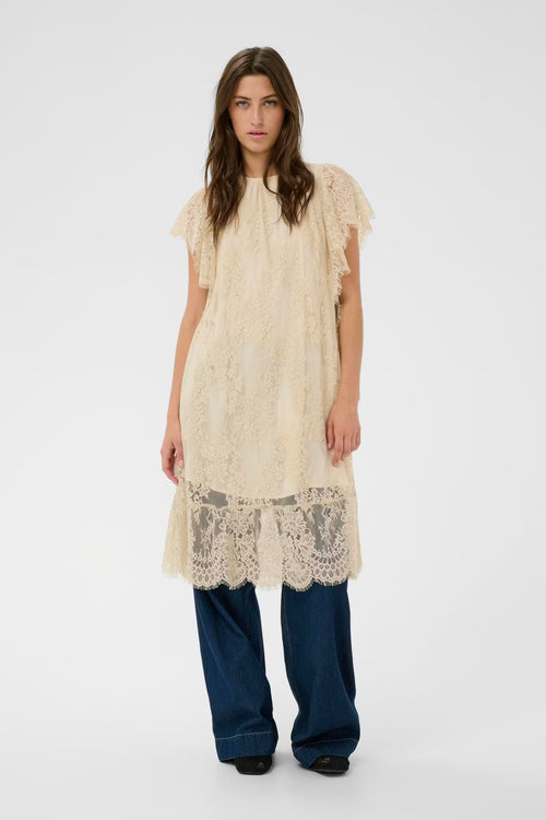 Woman wearing a beige lace dress with blue pants on a white background