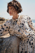 Woman wearing a floral dress sitting on a rock by the sea.