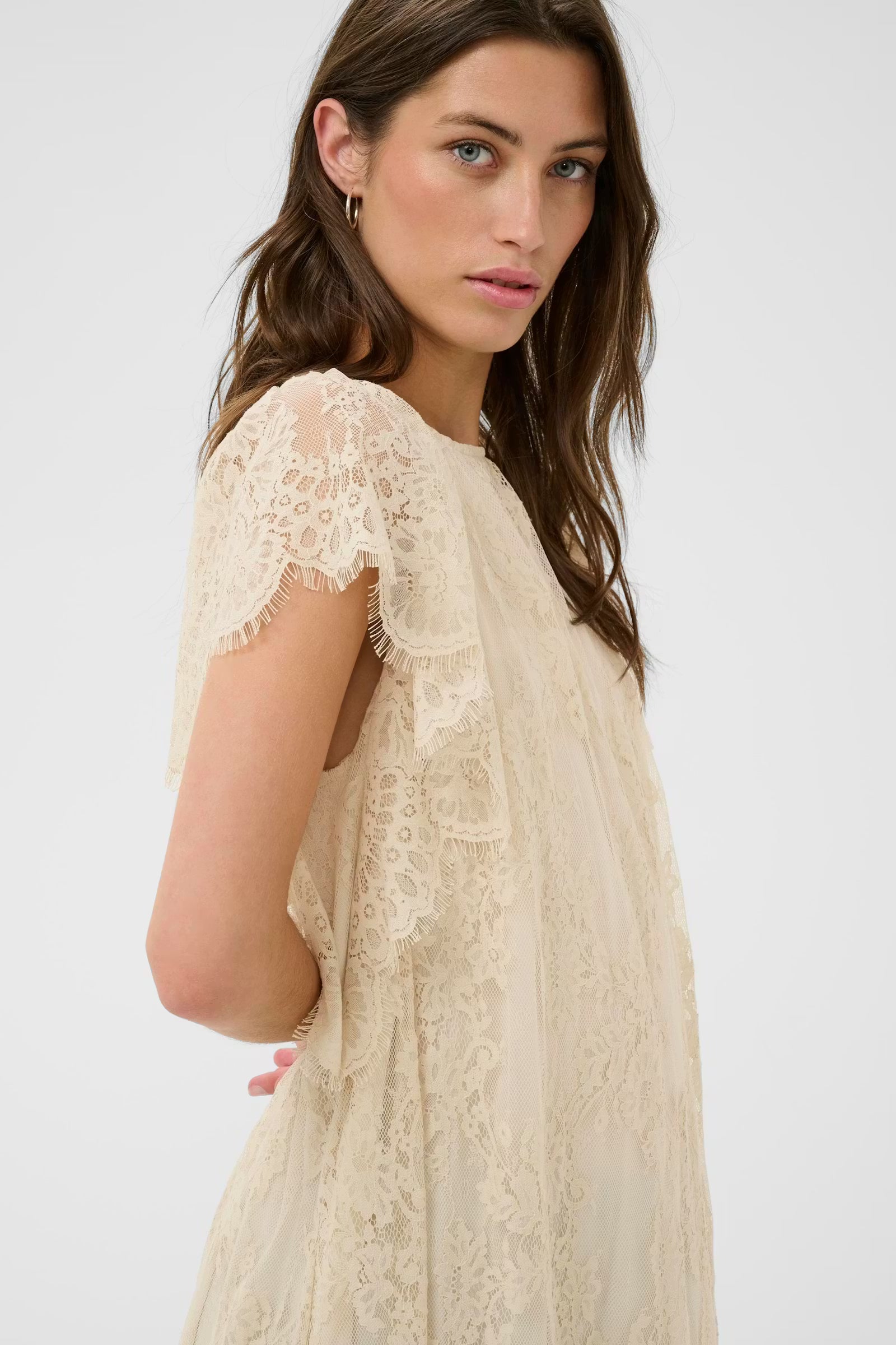 Woman wearing a beige lace dress against a white background