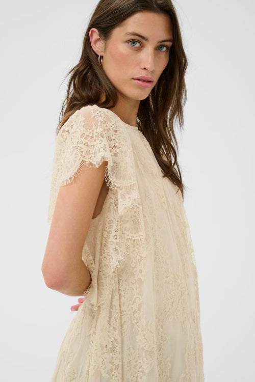 Woman wearing a beige lace dress against a white background
