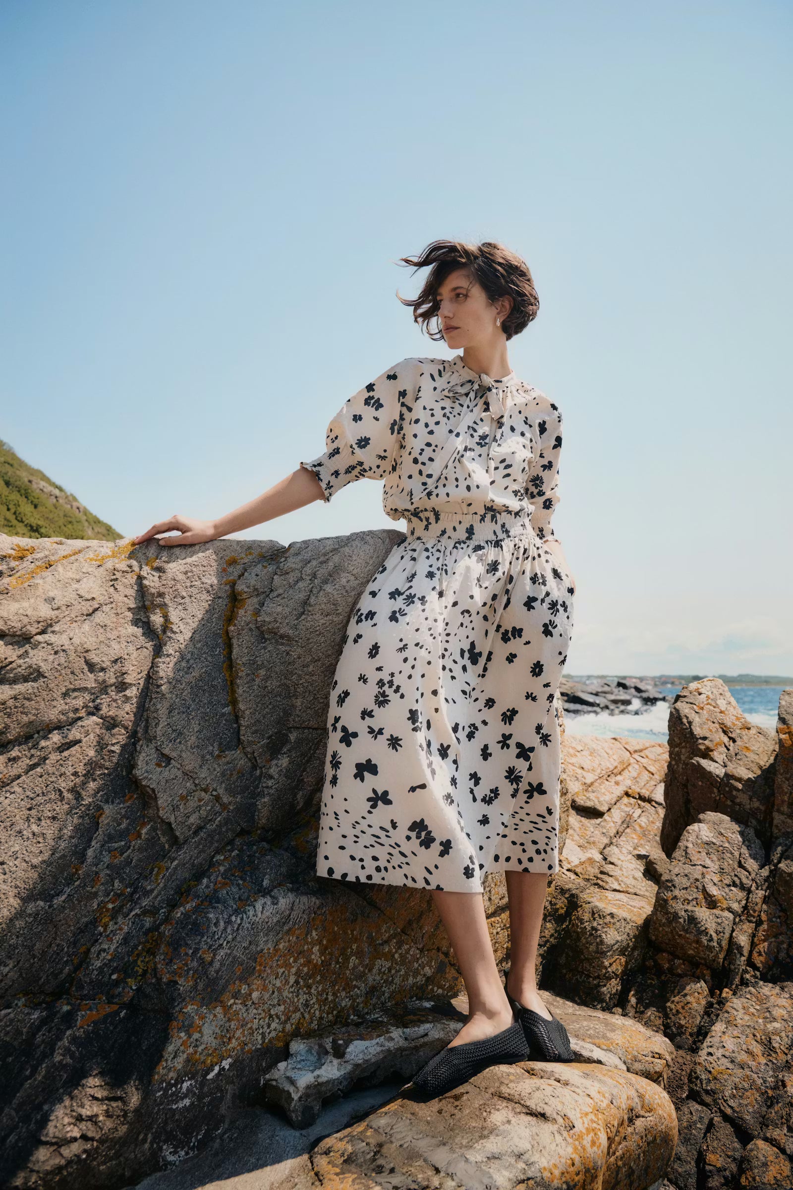 Woman in a floral dress standing on rocks by the sea