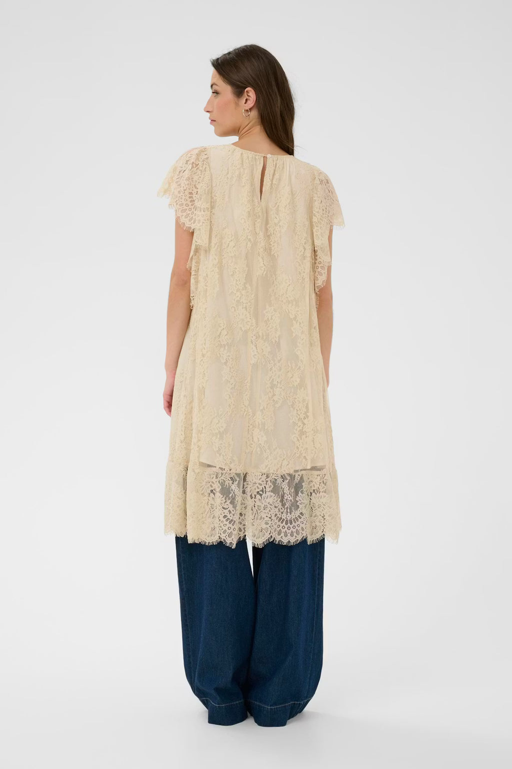 Woman wearing a cream lace top and blue pants on a white background