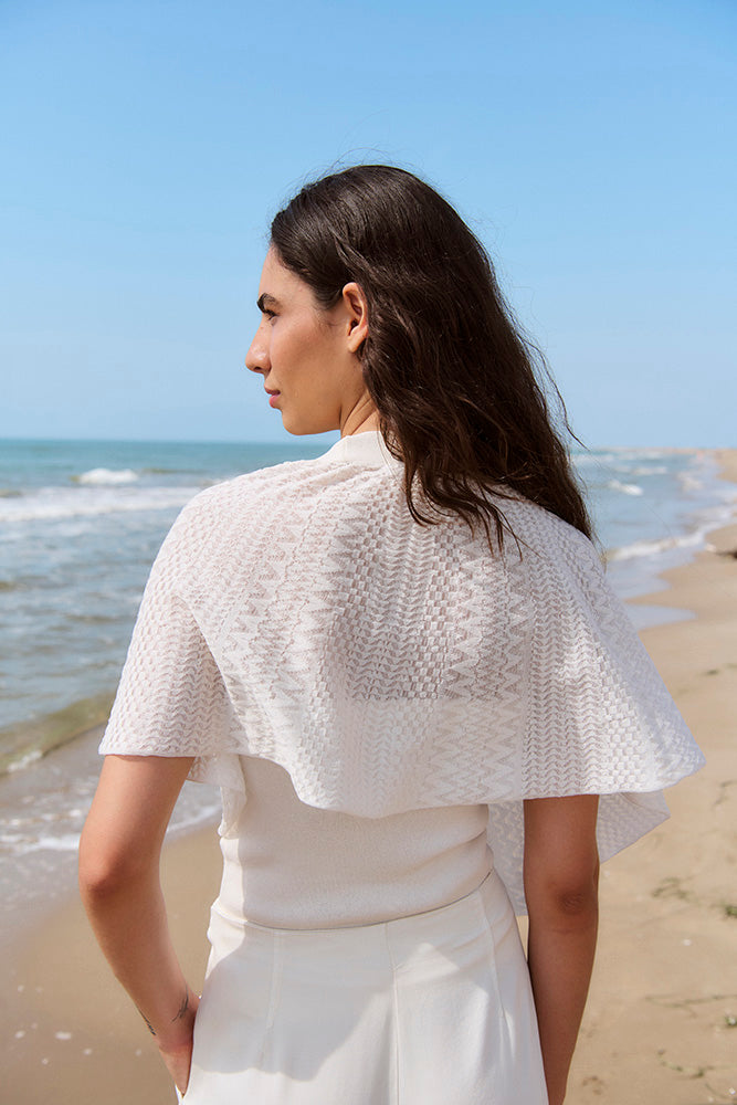Woman wearing a white textured shawl on a beach with ocean view