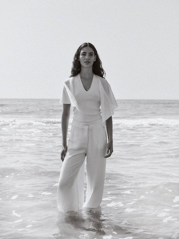 Woman in a white outfit standing in shallow water with a plain background