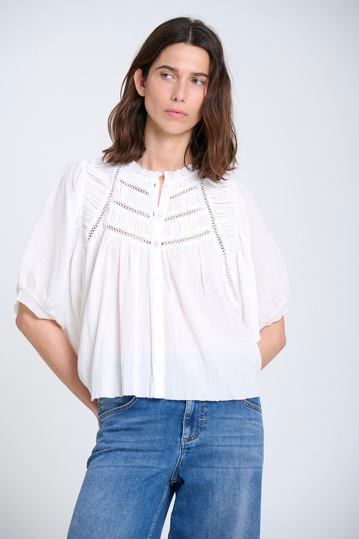 Woman wearing a white blouse and blue jeans against a plain background