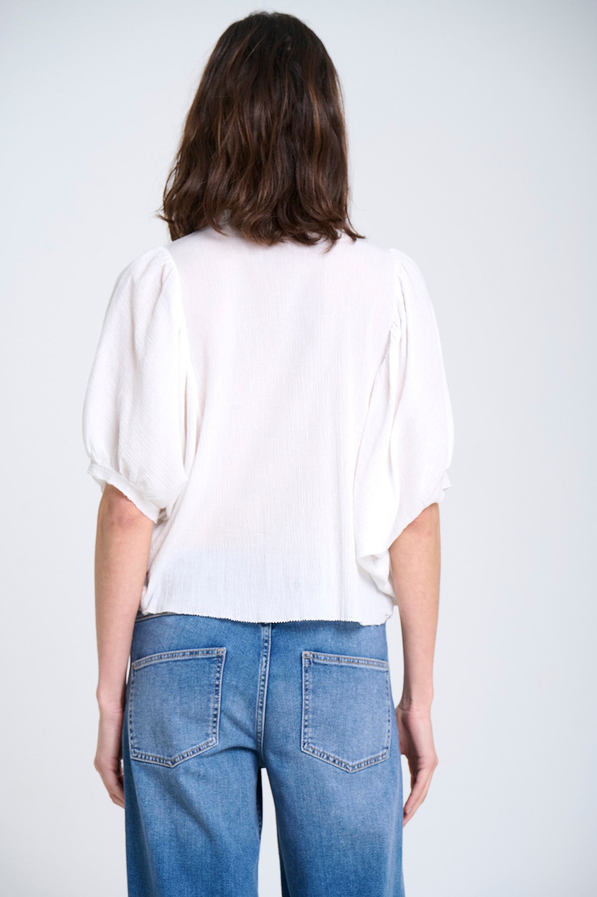 Person wearing a white peasant blouse and blue jeans on a plain background