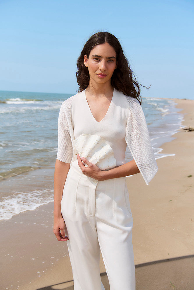 Woman in a white outfit standing on a beach with ocean waves in the background. all white outfit, euro summer outfit, what to wear to europe over 40 