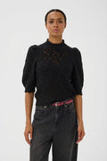 A model wearing a black lace knit mock-neck top with puffed 3/4 sleeves, paired with dark gray jeans and a pink belt, against a plain light gray background.
