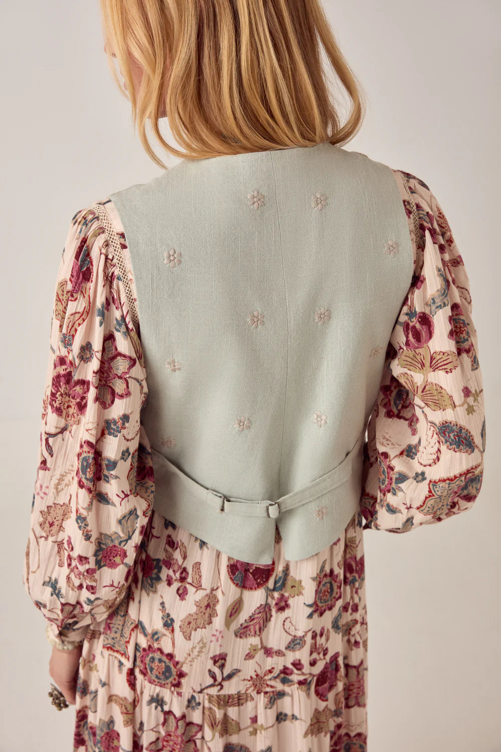 Person wearing a floral dress over a light green vest on a plain background