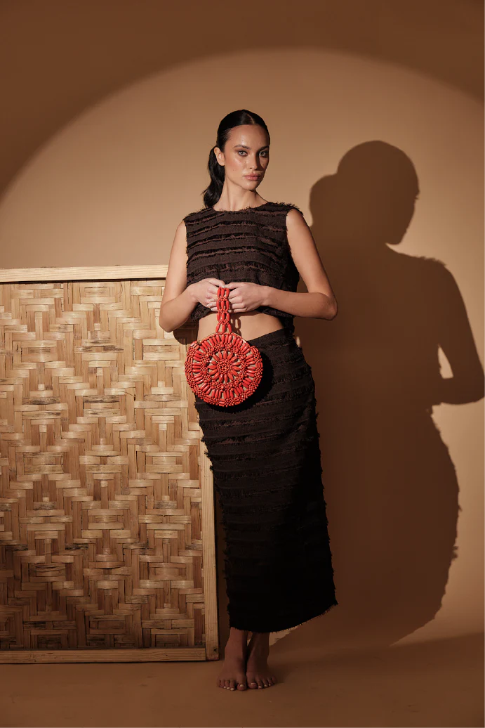 Woman holding a red beaded purse against a textured wall.
