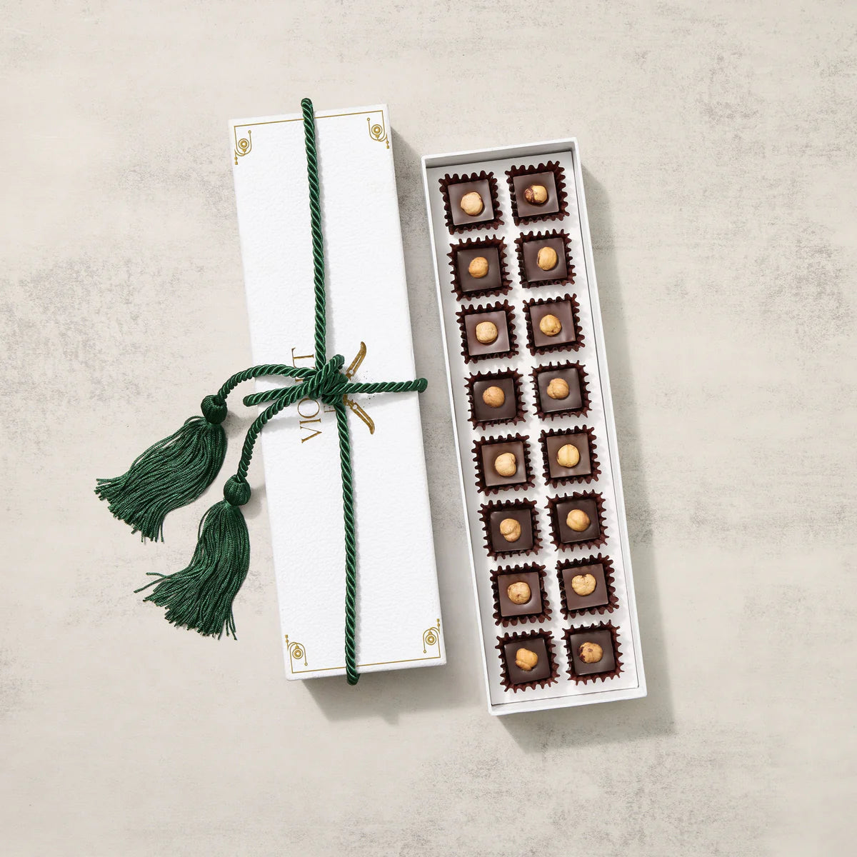 Box of chocolates with a decorative green ribbon on a light gray background