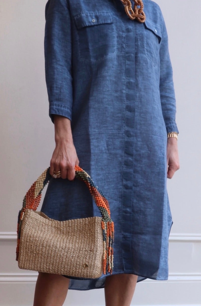 Person wearing a blue dress holding a woven handbag against a neutral background