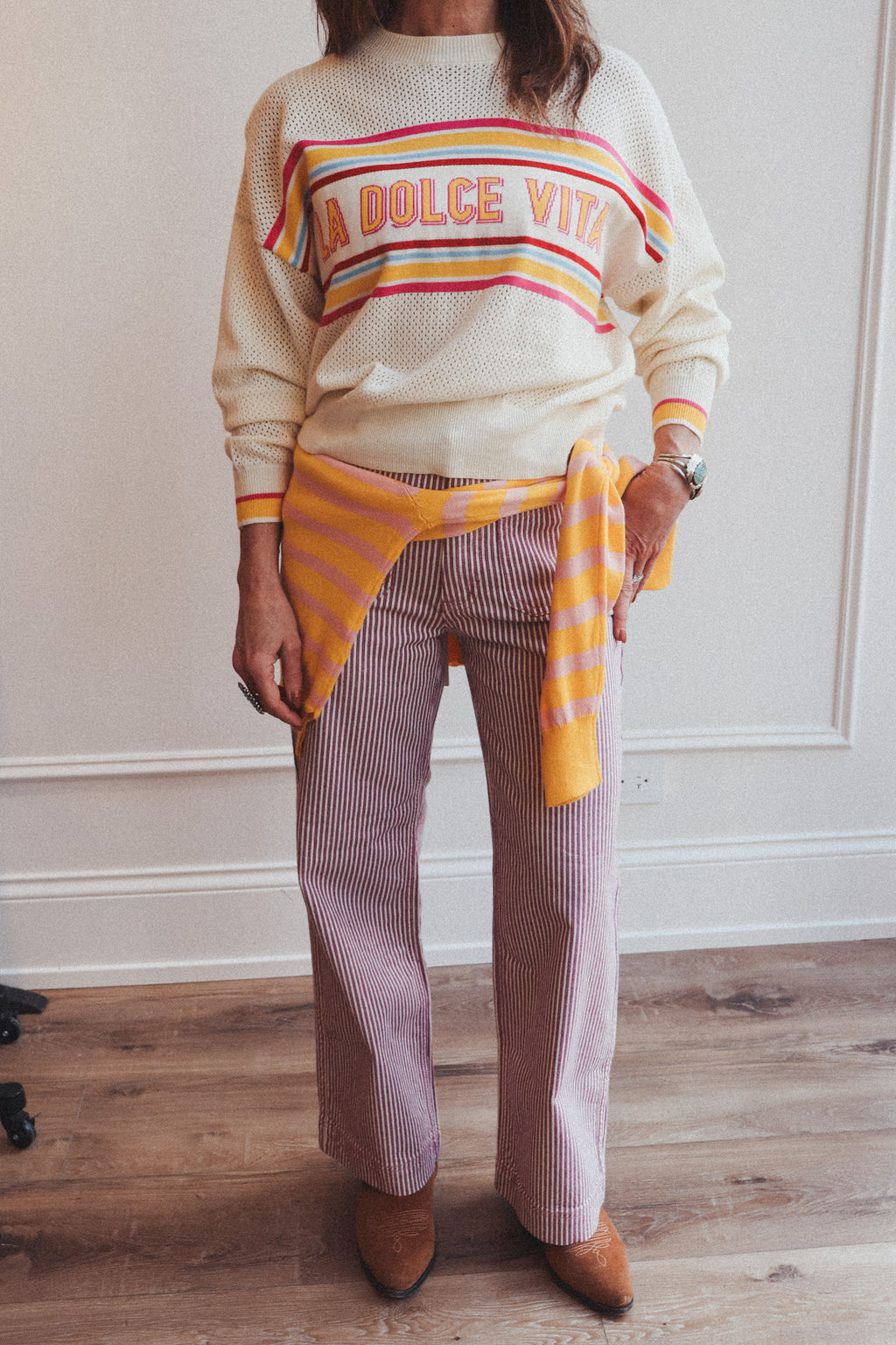 Person wearing a colorful sweater with text and striped pants indoors.
