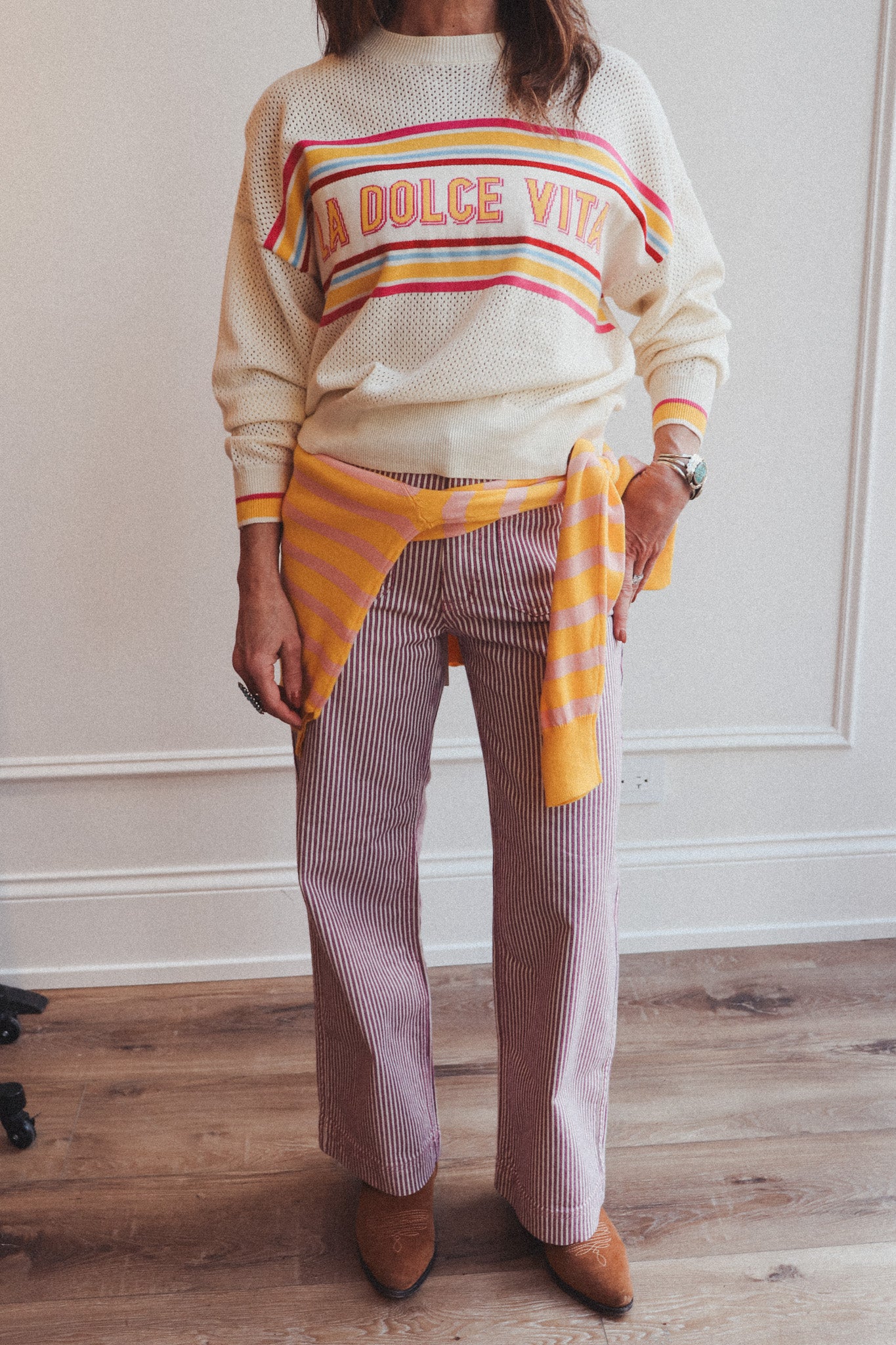 Person wearing a colorful sweater with text and striped pants indoors.