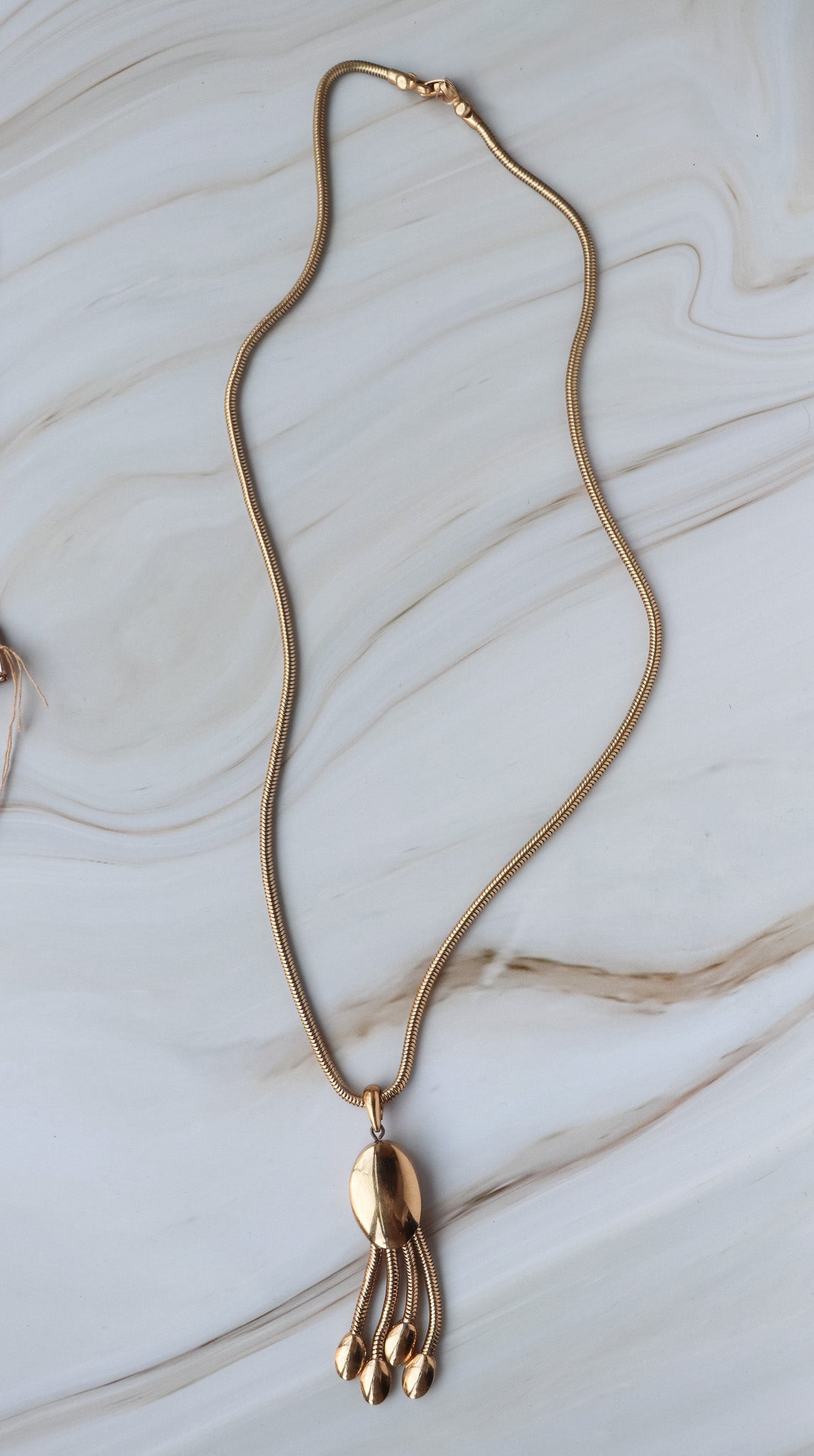 vintage Gold necklace with a unique fringe pendant on a marble surface