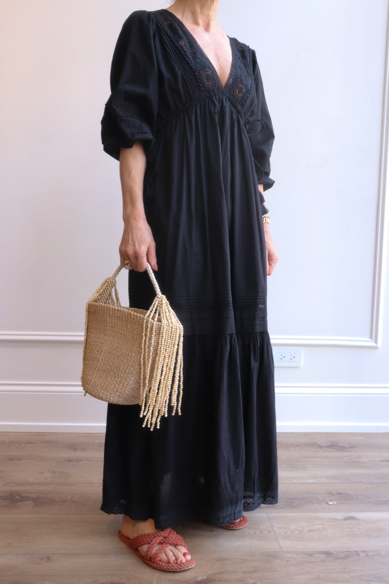 Person wearing a black dress holding a woven handbag indoors.