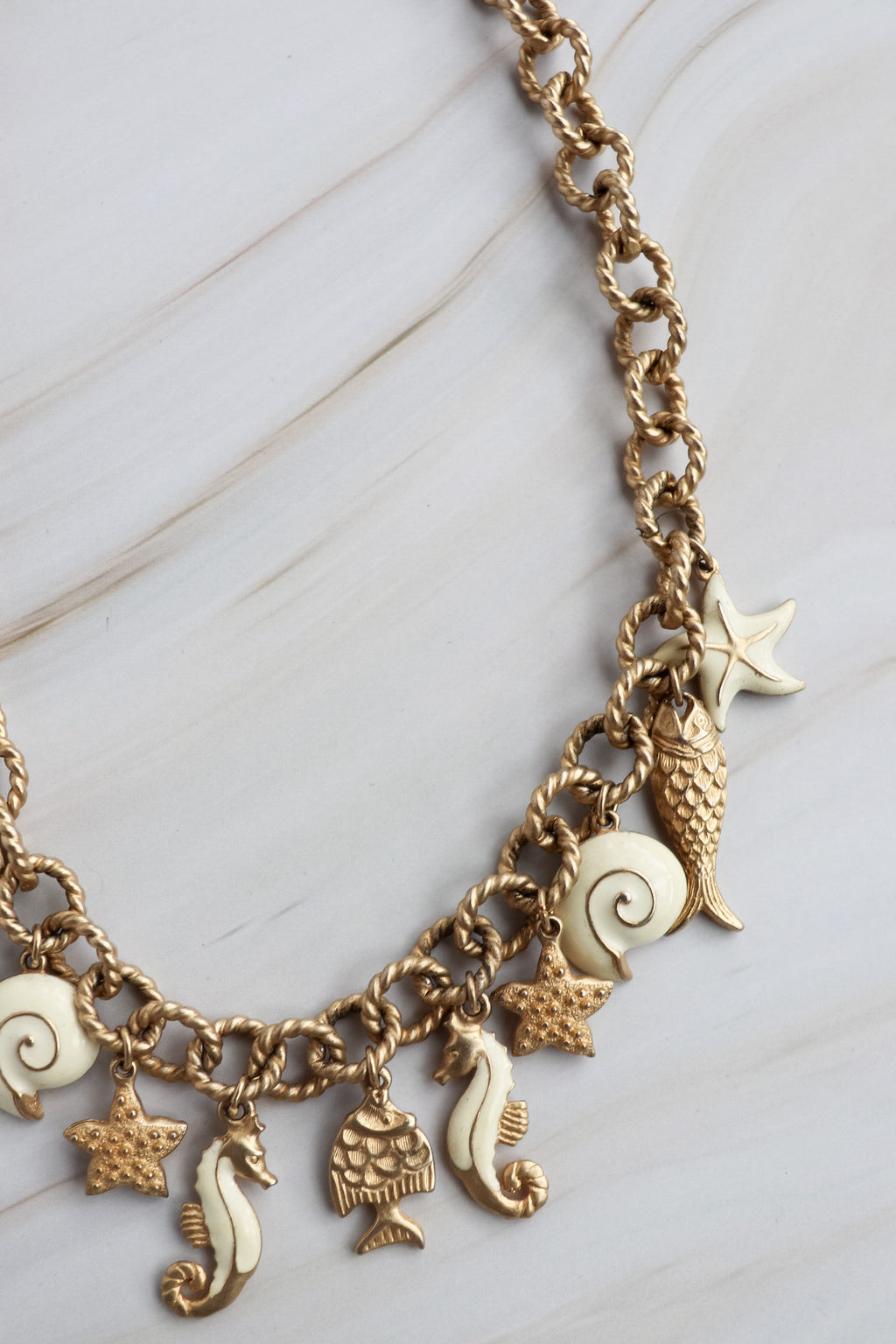 Gold charm bracelet with various sea-themed charms on a marble surface