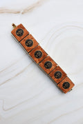 Bracelet with brown leather strap and black circular designs on a white marble surface