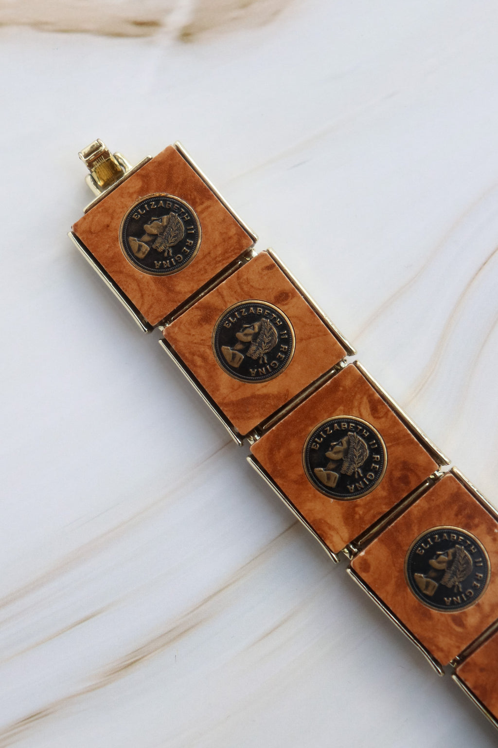 Bracelet with brown leather and bronze emblem design on a white marble surface