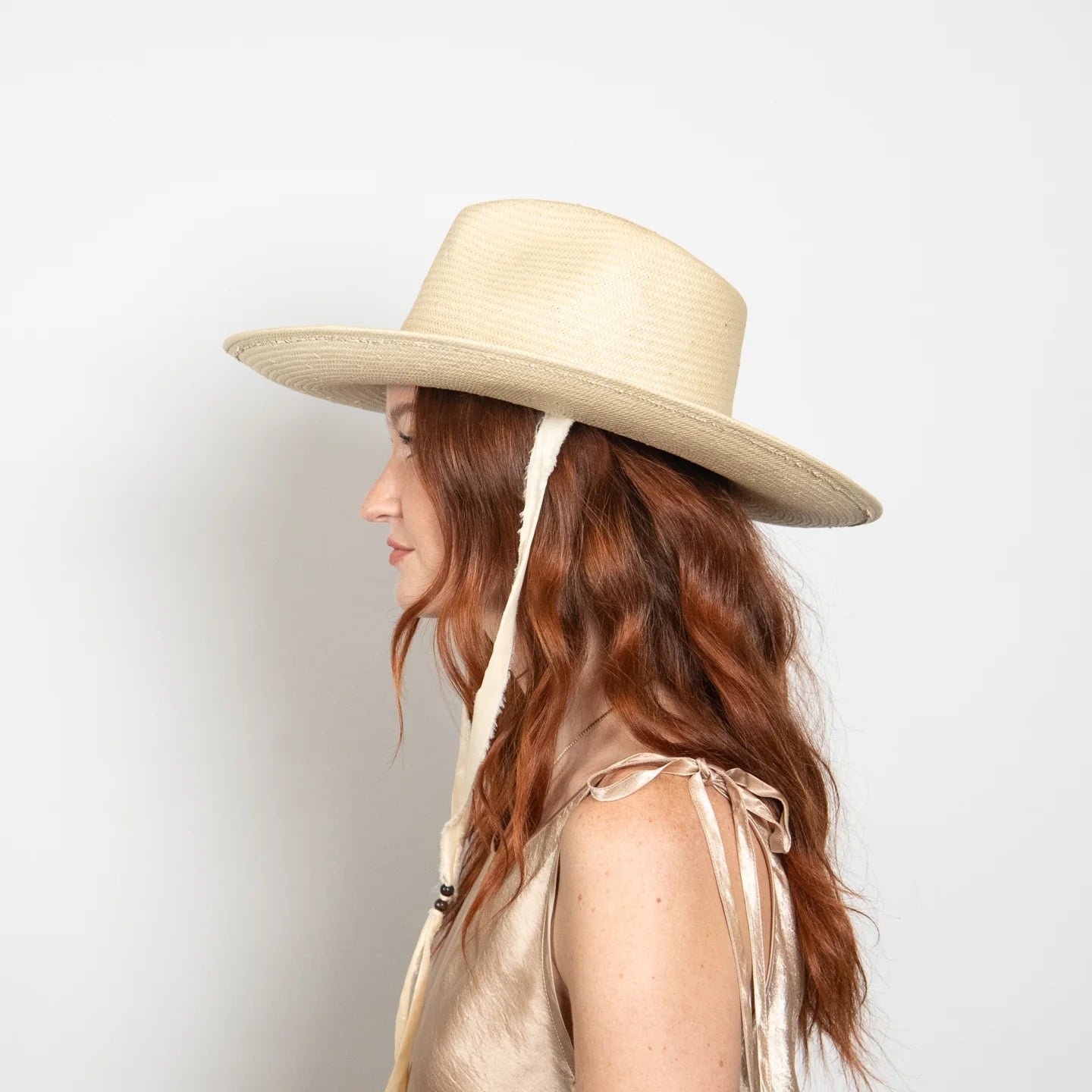 Woman wearing a beige wide-brimmed hat with a ribbon on a light gray background