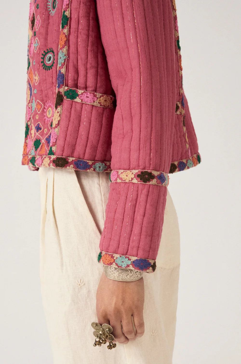 Close-up of a pink embroidered traditional outfit with white pants on a plain background