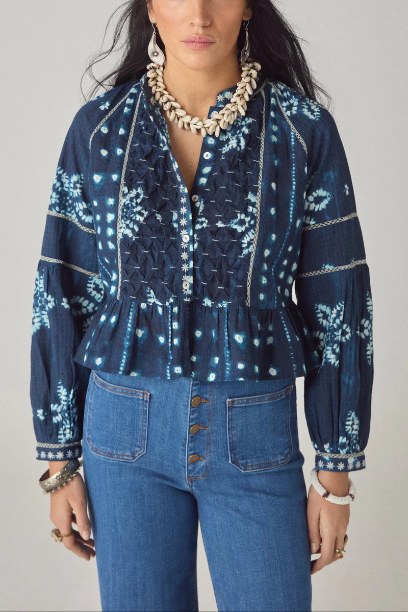 Woman wearing a blue patterned blouse and jeans against a gray background