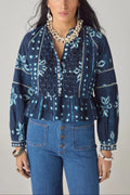Woman wearing a blue patterned blouse and jeans against a gray background