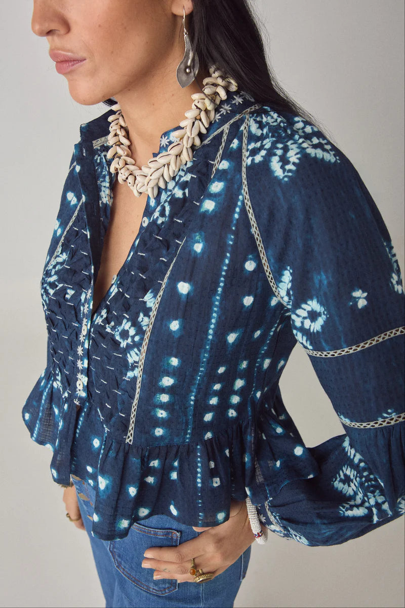 Woman wearing a blue patterned blouse with ruffled sleeves on a gray background