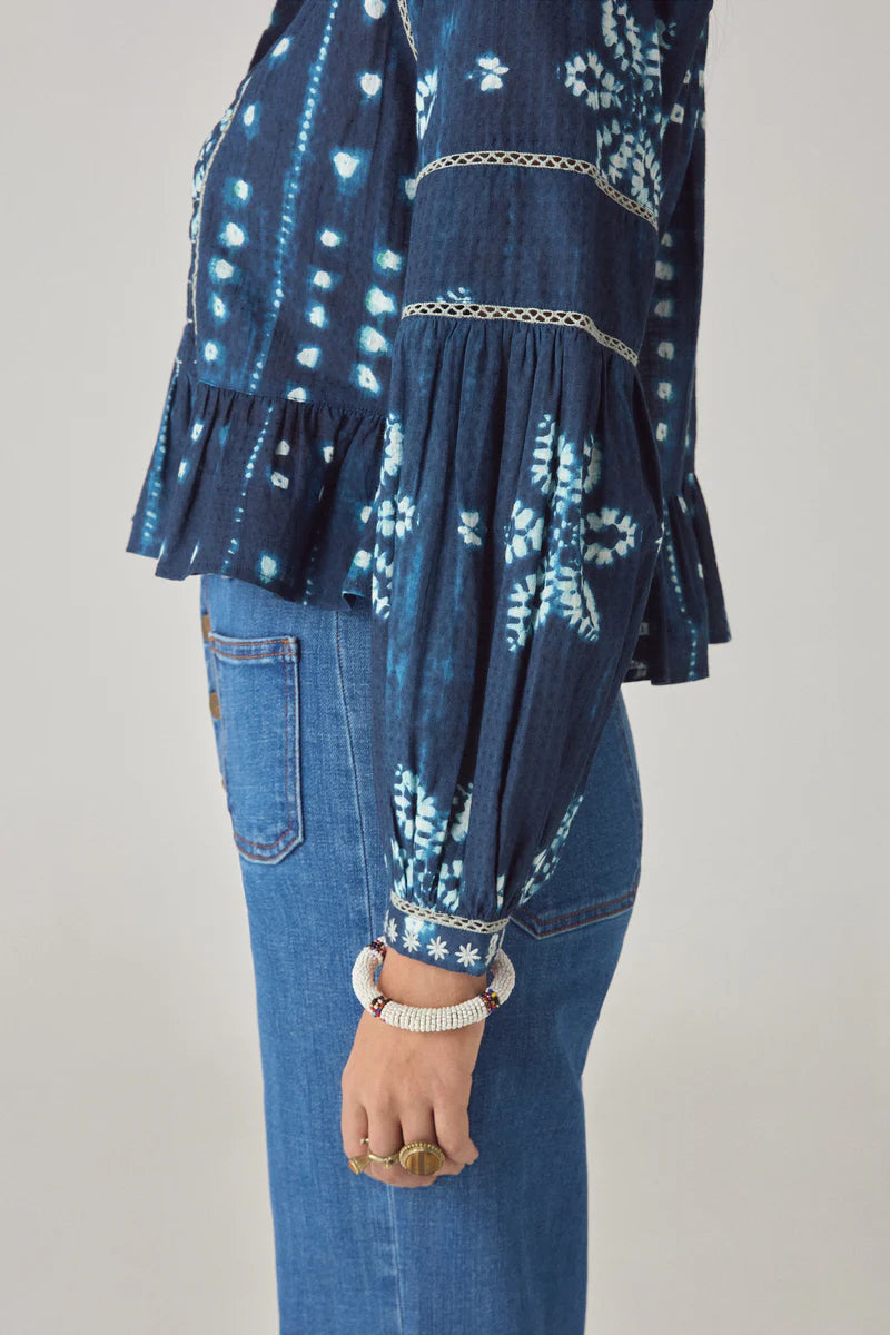 Person wearing a blue patterned top and jeans on a plain background
