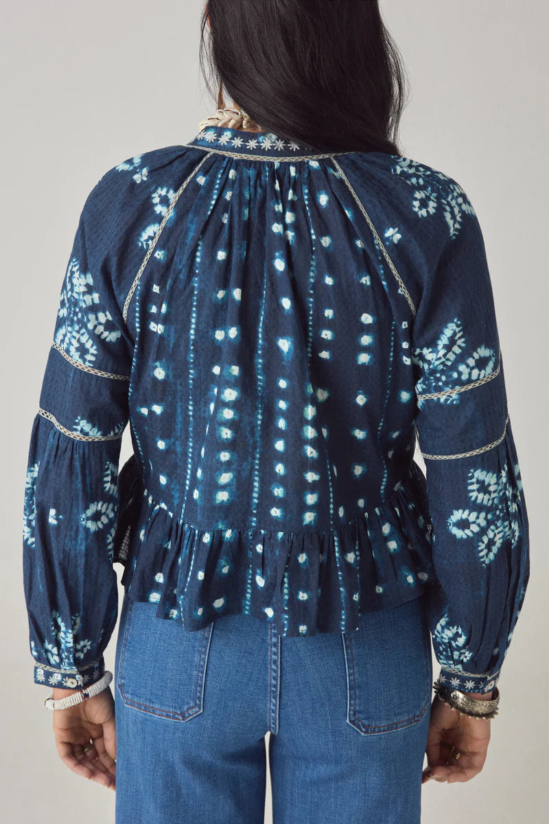 Person wearing a blue patterned blouse and jeans on a plain background