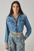 Woman wearing a blue denim shirt with floral patterns and a patterned skirt on a gray background