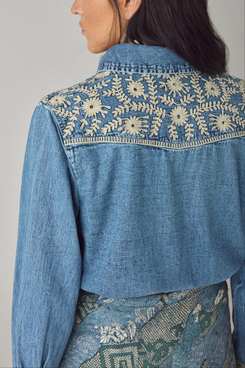 Blue denim jacket with floral embroidery on a plain background