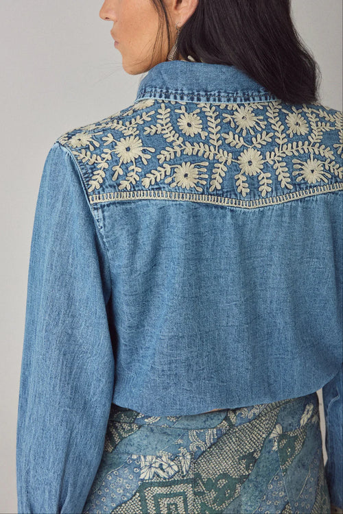 Blue denim jacket with floral embroidery on a plain background