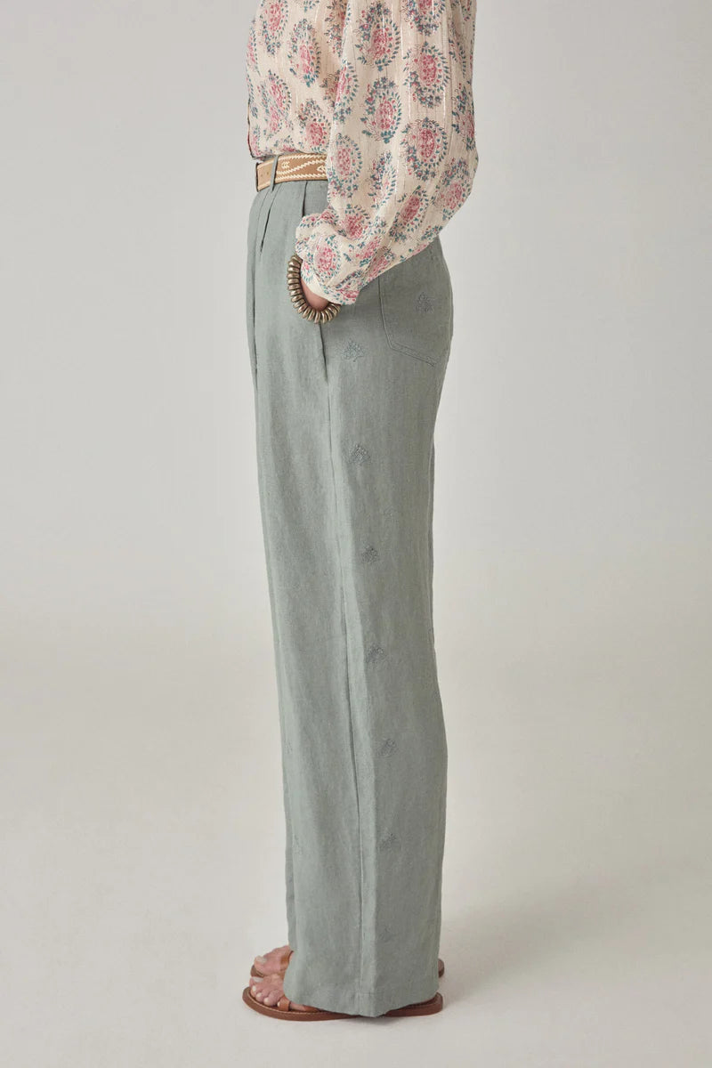 Person wearing a patterned blouse and light gray pants on a plain background