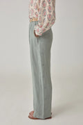 Person wearing a patterned blouse and light gray pants on a plain background