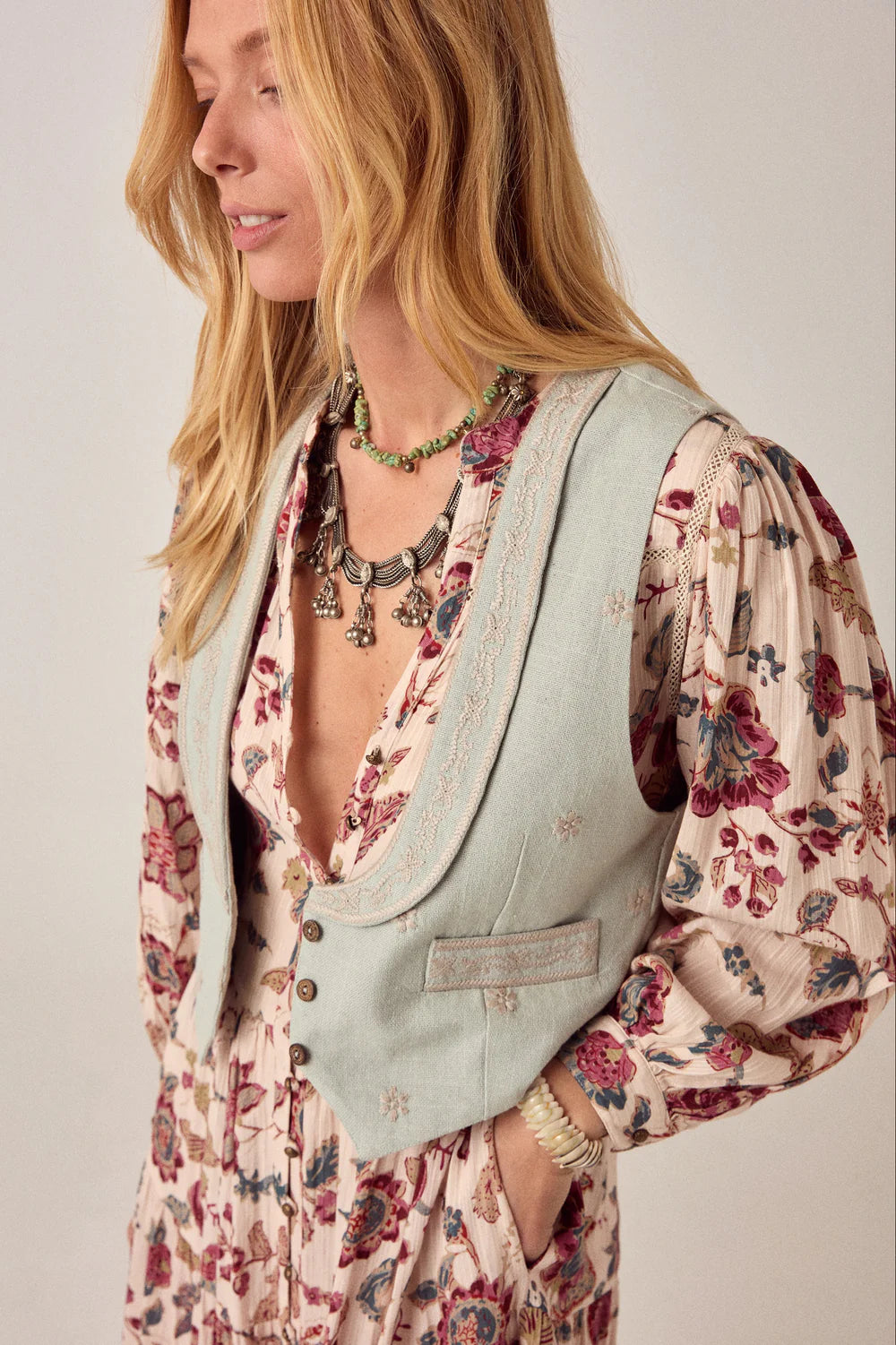 Woman wearing a floral dress with a light blue vest against a plain background