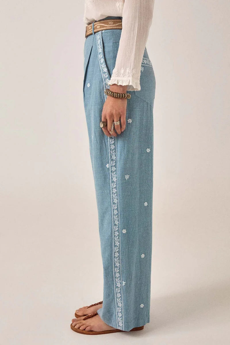 Light blue denim pants with white button details on a plain background