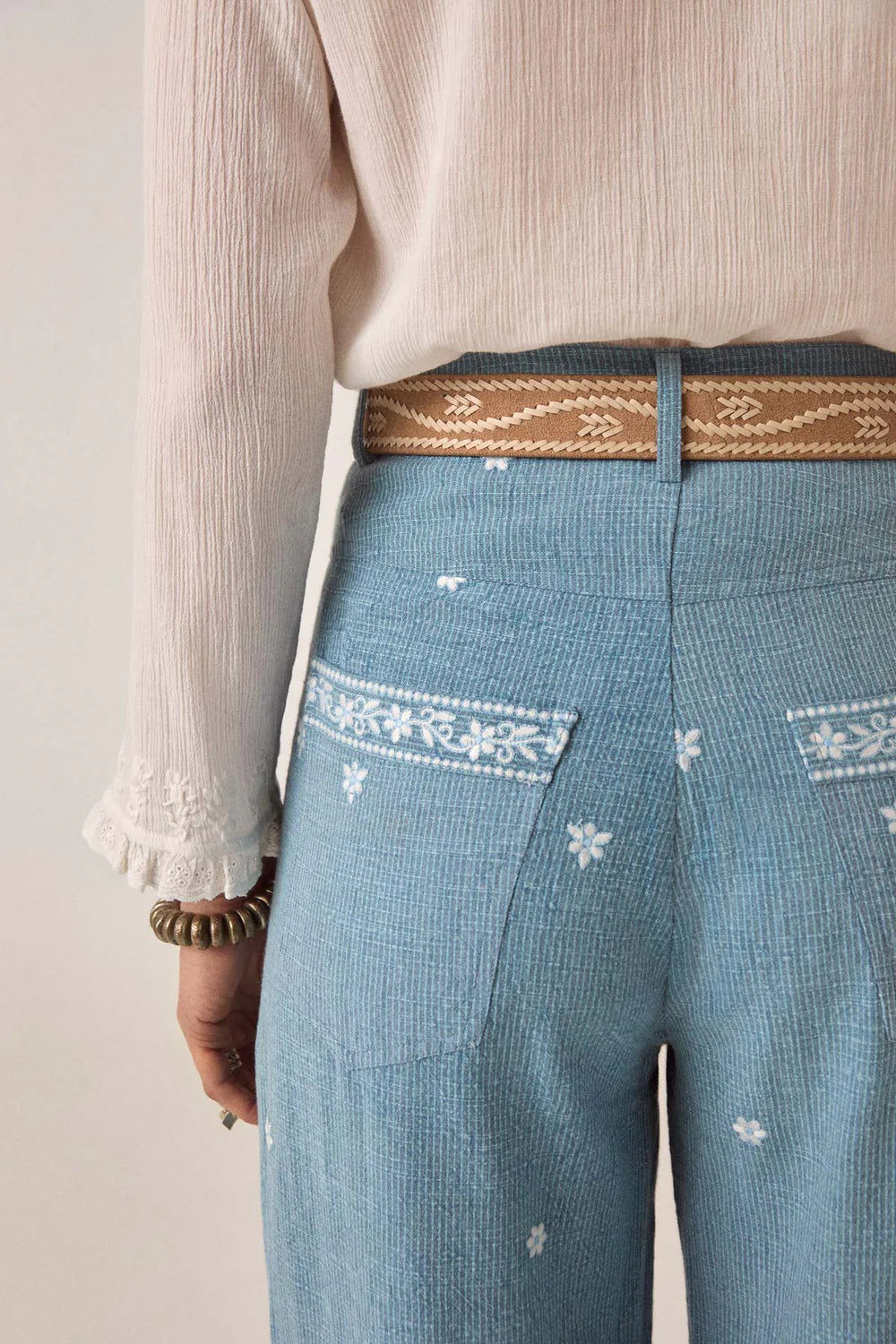 Blue pants with white floral embroidery and a brown belt worn by a person.