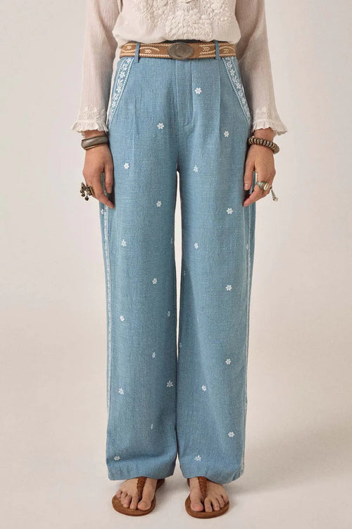 Person wearing light blue denim pants with white floral patterns on a plain background. Western bottoms, western trousers, western pants 