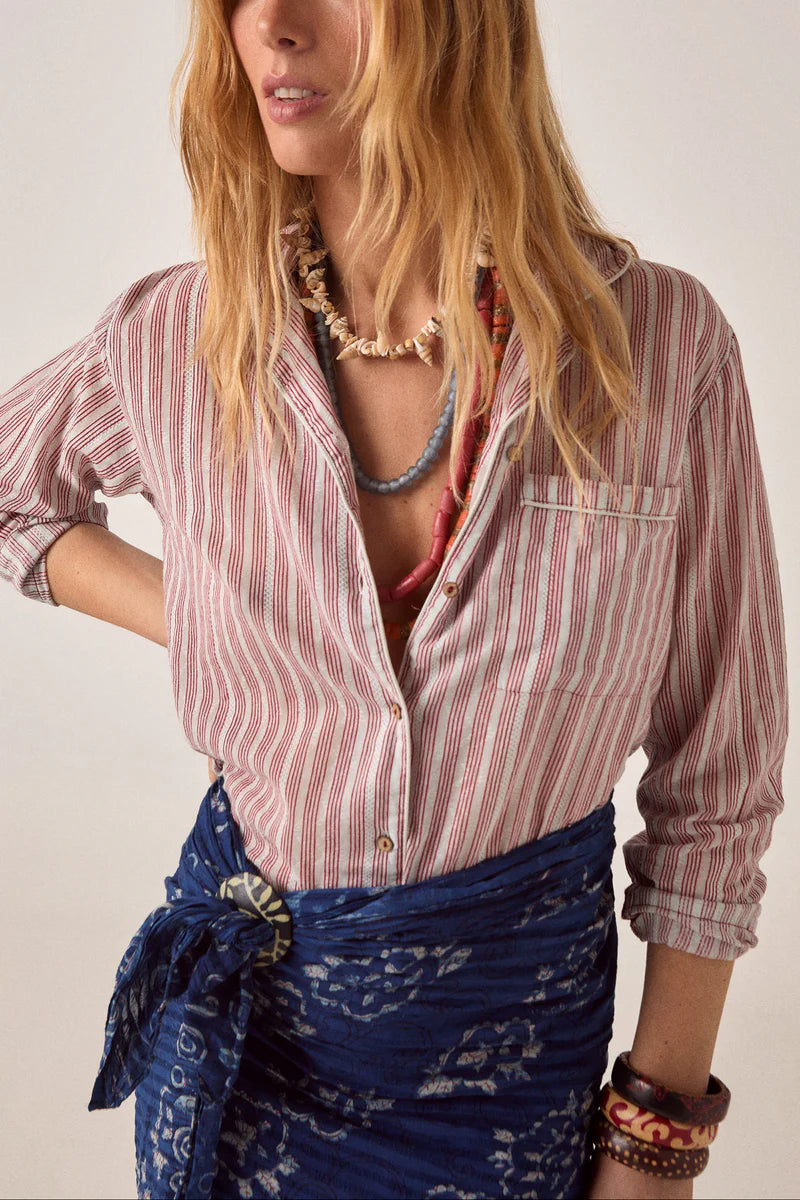 Woman wearing a striped shirt and blue patterned skirt with a plain background