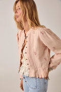 Woman wearing a light pink blouse with floral patterns on a plain background