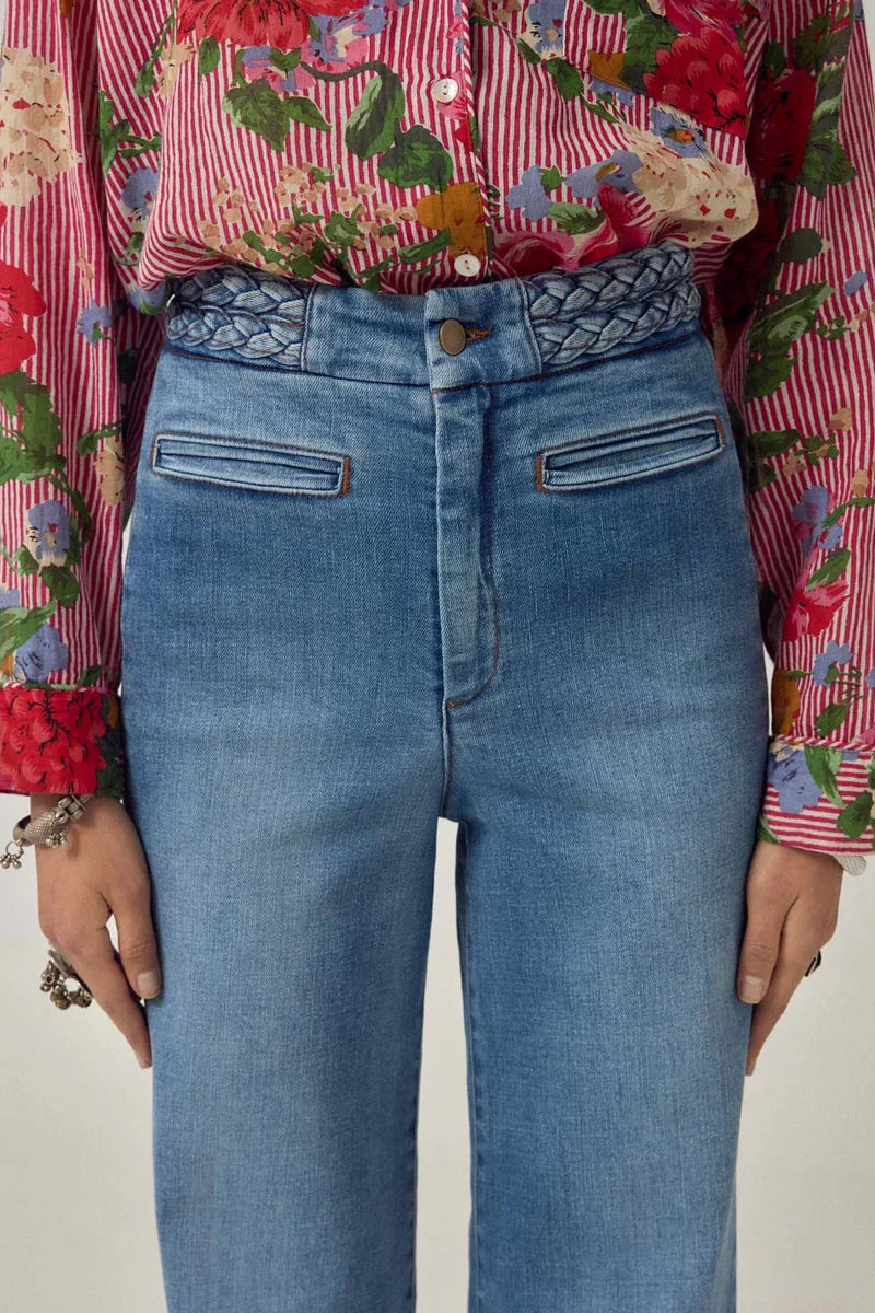 Person wearing a floral shirt and blue jeans with a plain background