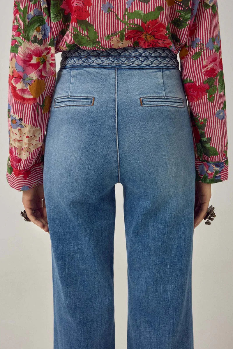 Person wearing a colorful floral blouse and blue jeans on a plain background