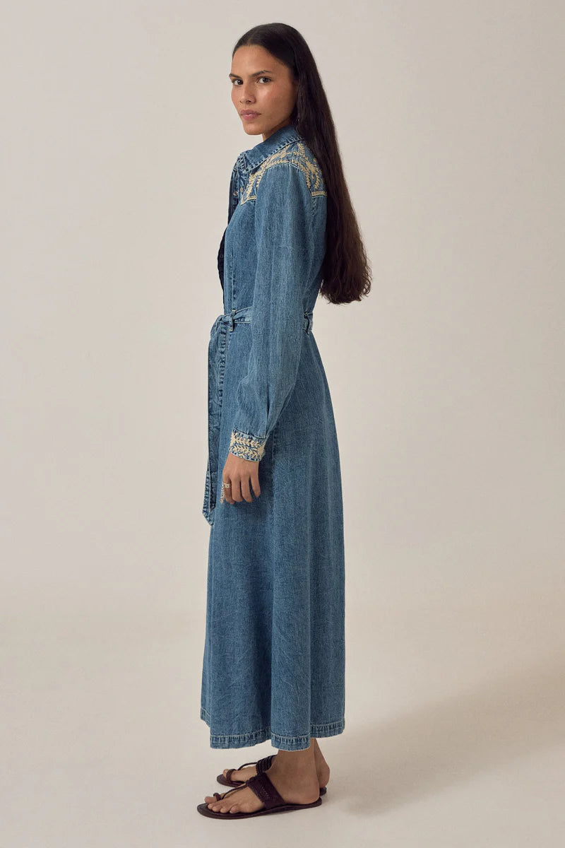 Woman wearing a long denim dress with lace details on a plain background