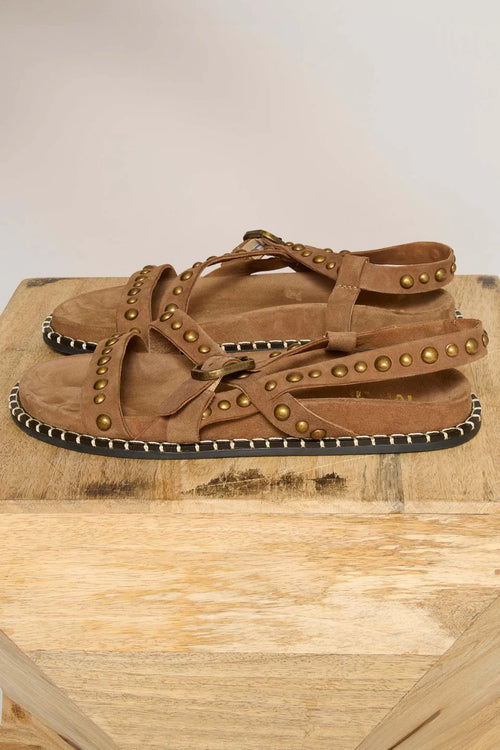 Brown sandal with decorative studs on a wooden surface