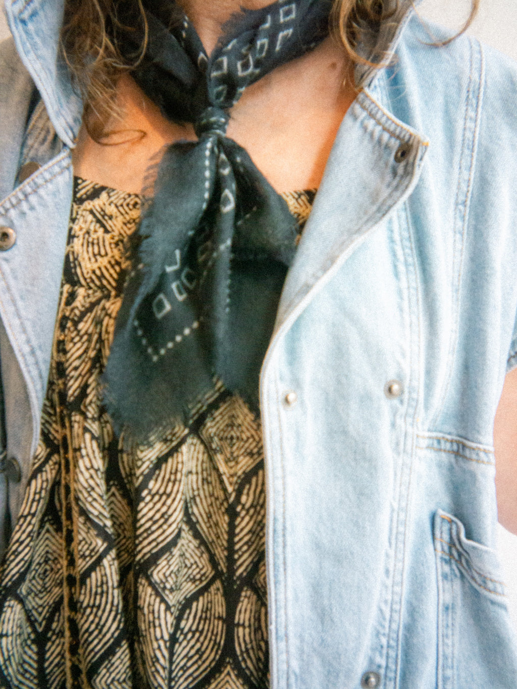 Person wearing a patterned neck scarf and denim vest jacket