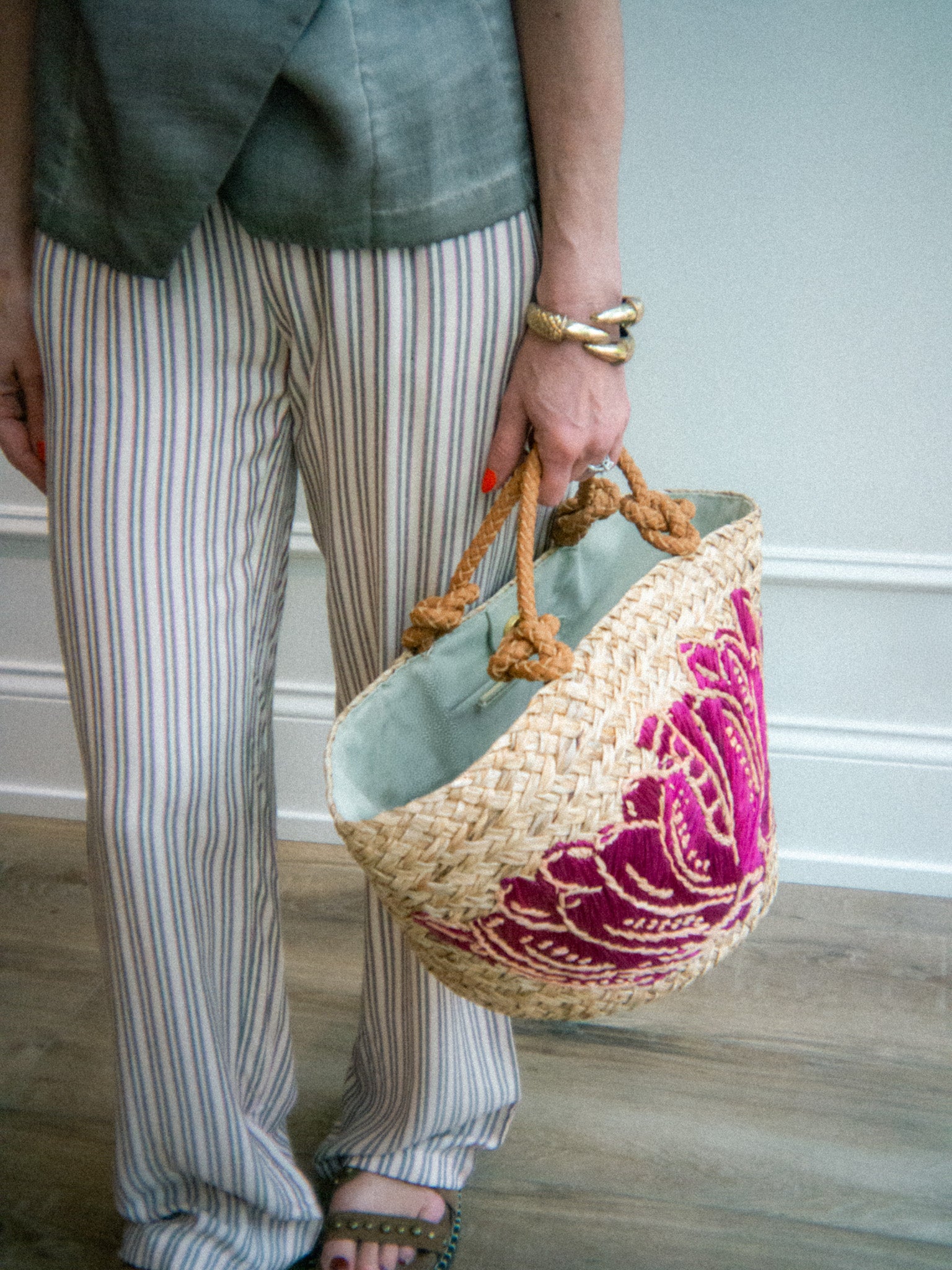 Person holding a woven bag with a pink floral pattern, wearing striped pants and a linen flowy vest top.